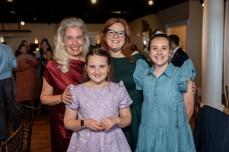 Four women and a girl pose together at The White Room, with warm overhead lighting and guests mingling in the background.