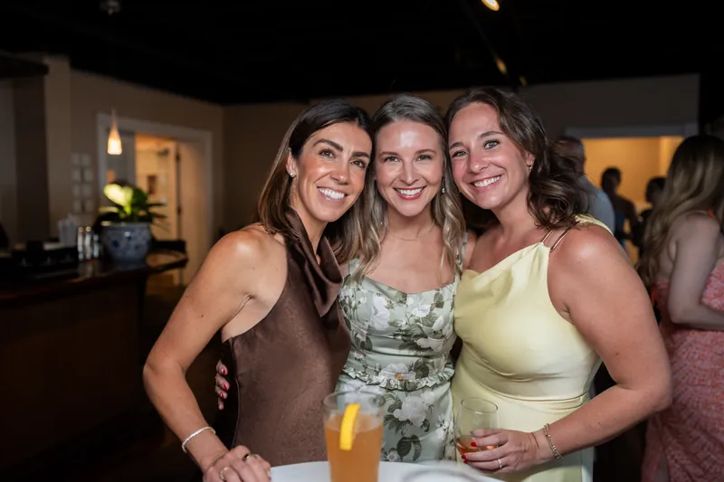 Three women smile at the camera while holding drinks at The White Room's reception.