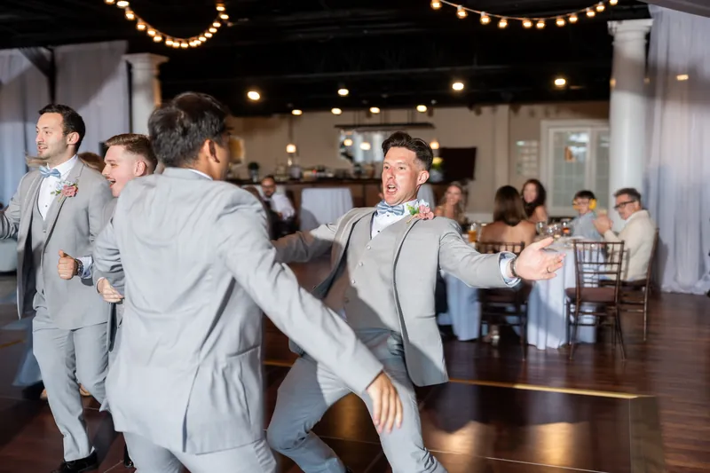 Men in gray suits dance and celebrate together on the dance floor at The White Room.