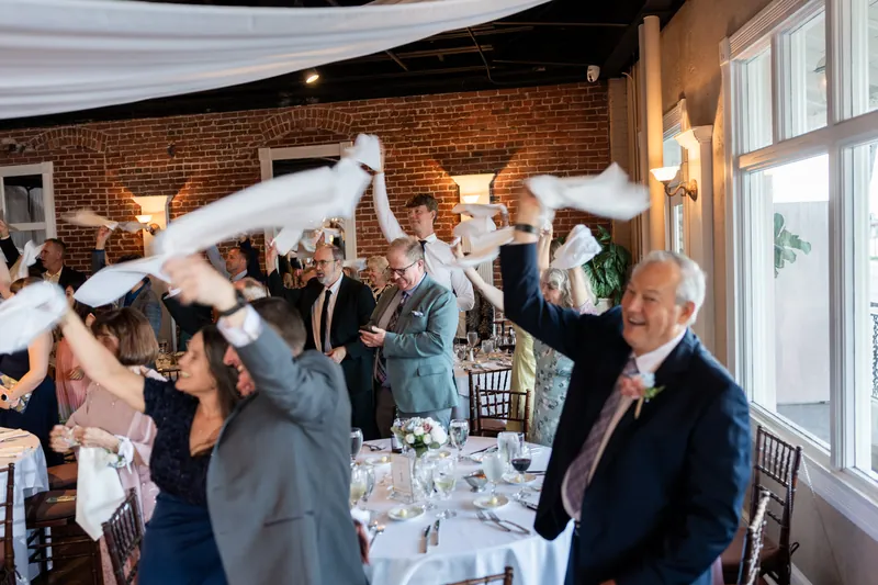 Guests toss white napkins in the air during a lively moment at The White Room's brick-lined reception space.