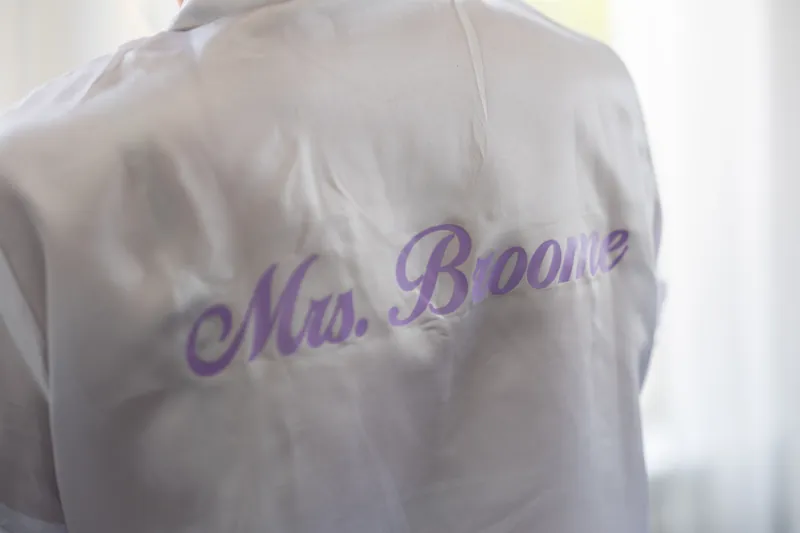 Close-up of a white button-up shirt embroidered with "Mrs. Boone" in purple script on the back.