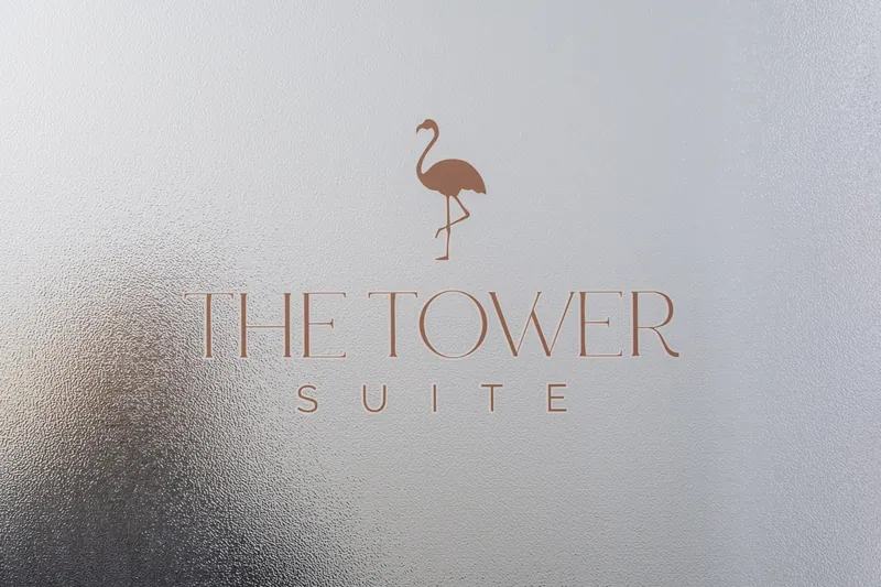 The Tower Suite logo featuring a flamingo and serif lettering displayed on frosted glass.