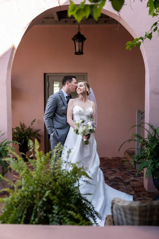 Tim and Sarah stand close together under a terracotta archway framed by green foliage.