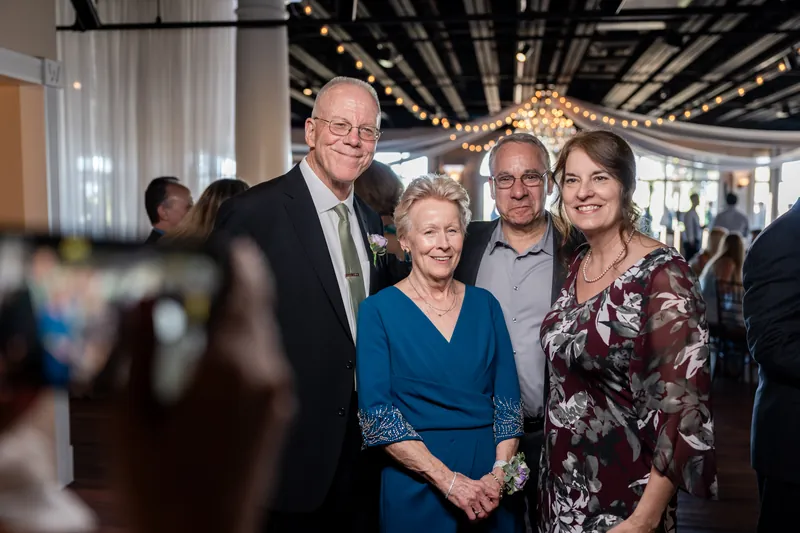 Four family members pose together indoors at the reception, with string lights and draped white fabric overhead.