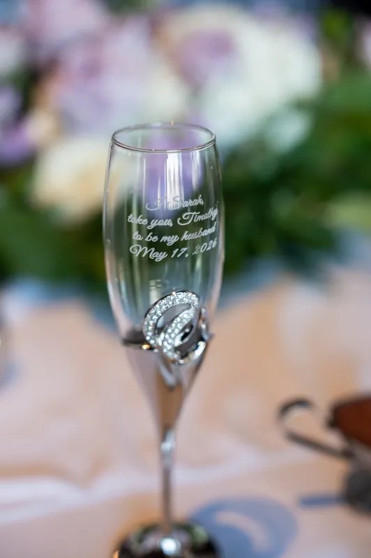 Engraved champagne flute with Sarah and Tim's names and wedding date, with a diamond ring resting against the glass stem.