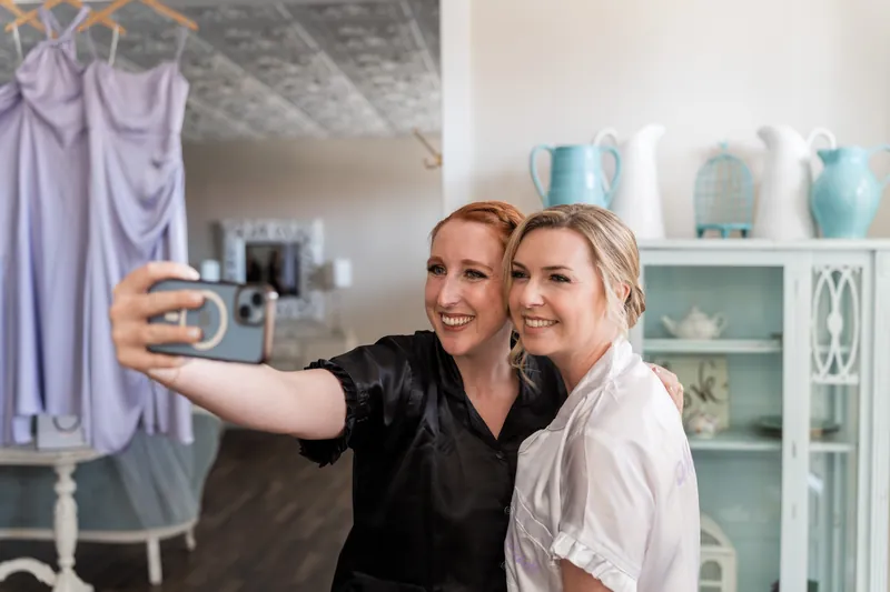 A woman in black takes a selfie with Sarah in white at The White Room, shelving behind them.