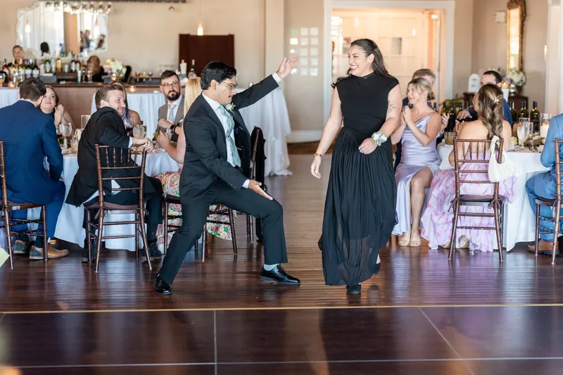 Wedding guests dance on the wooden floor while Sarah in a black dress and Tim in a suit move across the dance floor.