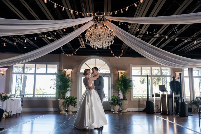Sarah and Tim embrace while dancing, framed by the ornate venue's arched windows and flowing white ceiling fabric.