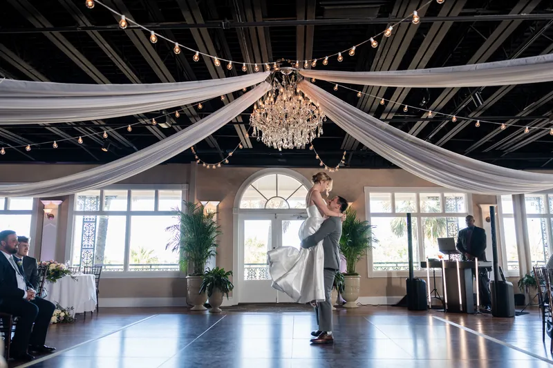 Sarah and Tim exchange vows beneath draped fabric and a crystal chandelier in The White Room's sunlit ballroom.