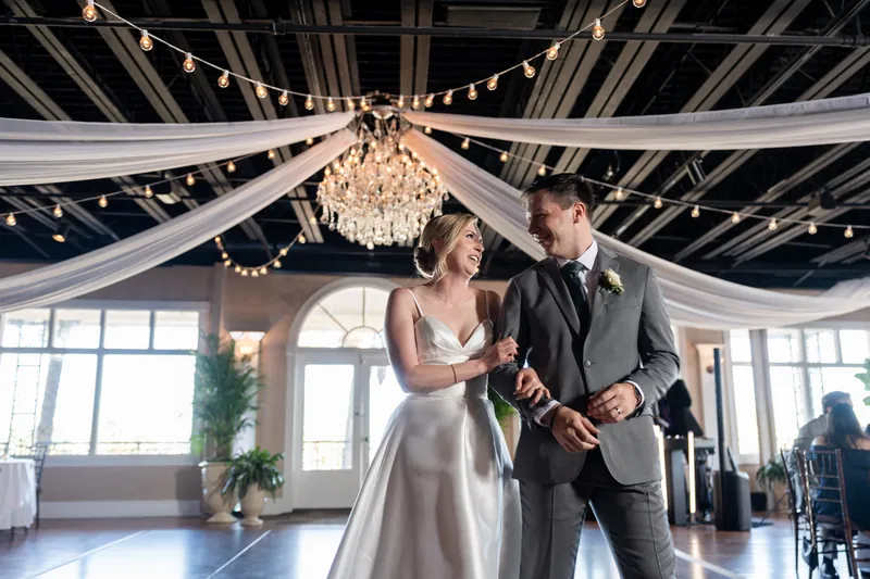 Tim and Sarah hold hands and smile at each other during their ceremony, with string lights and greenery framing the space.