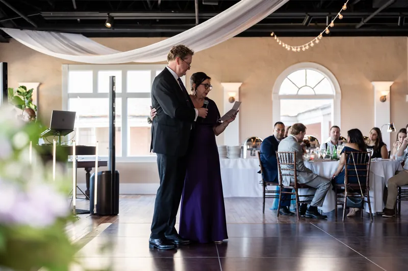 Tim leads Sarah in a dance across the polished floor as seated guests observe in the elegant venue.