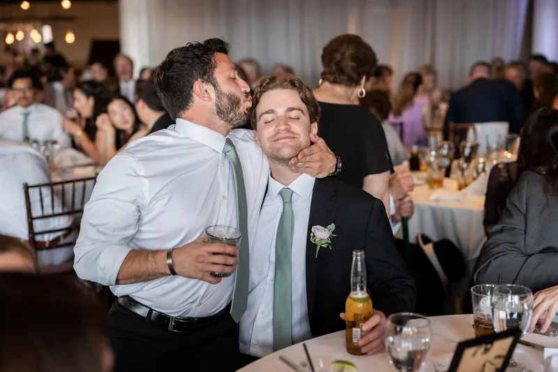 Tim embraces a guest at a reception table while wearing a light blue shirt and green boutonniere.