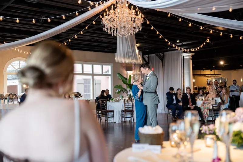 A guest in the foreground watches as Sarah and Tim embrace during their first dance beneath the chandelier.