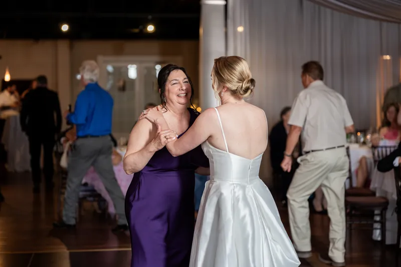 Sarah dances with a guest in a purple dress while others move across the wooden floor around them.