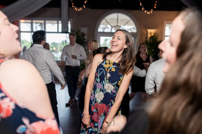 A woman in a floral navy dress laughs and dances surrounded by other celebration guests.