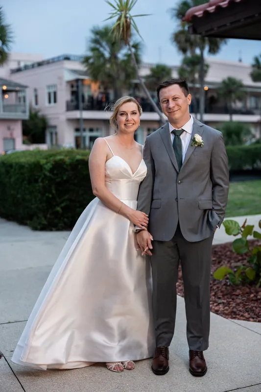 Sarah and Tim stand holding hands on a tree-lined street in Downtown St. Augustine, Sarah in an ivory gown and Tim in a gray