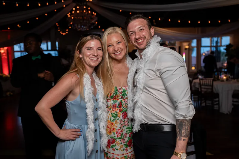 Sarah poses between two guests under warm string lights, all three smiling at the camera with the reception space visible