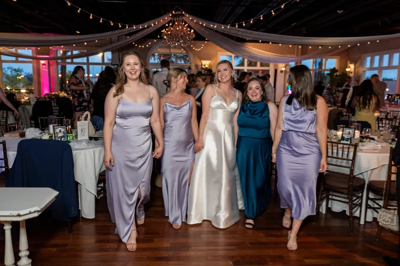 Sarah walks down the dance floor flanked by five attendants in matching lavender gowns, with decorated ceilings and tables