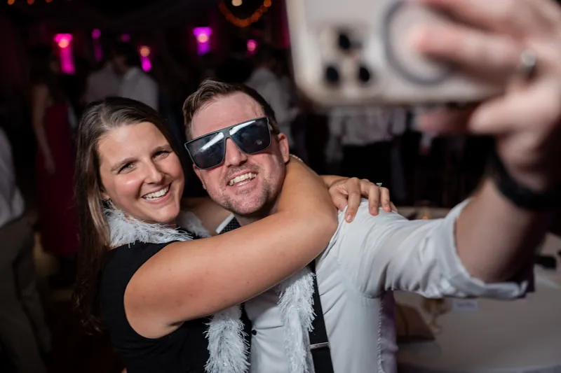 Sarah and Tim take a selfie on the dance floor, both smiling at the camera with colorful lights glowing.