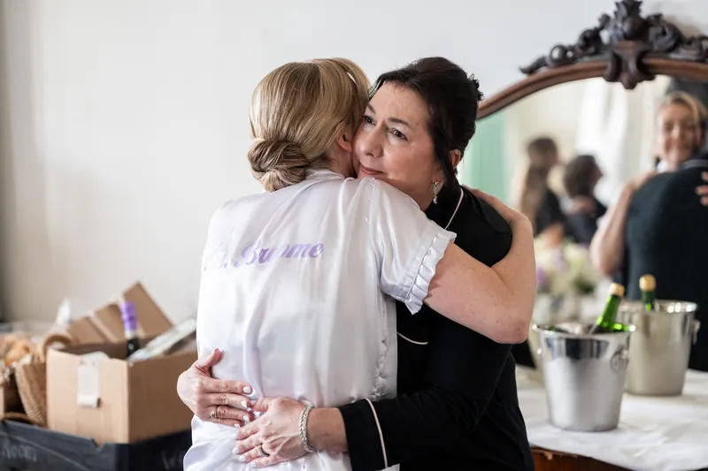 Sarah embraces a woman in a white shirt with "bride" written on the back in an intimate moment at The White Room.