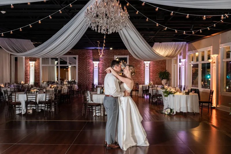 Sarah and Tim dance together at The White Room, surrounded by string lights and draped fabric, with reception tables