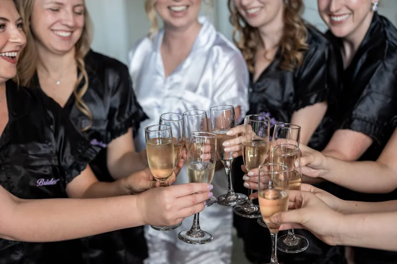 Five women in black robes raise champagne flutes together, celebrating with genuine smiles and laughter.