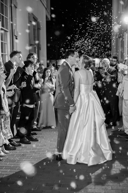 Black and white image of Sarah and Tim dancing outdoors at The White Room, with guests lined up on either side and confetti