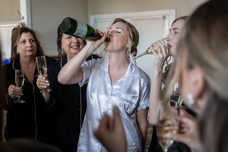 Sarah in a light blue shirt laughs as friends adjust her hair and makeup during pre-wedding celebrations.