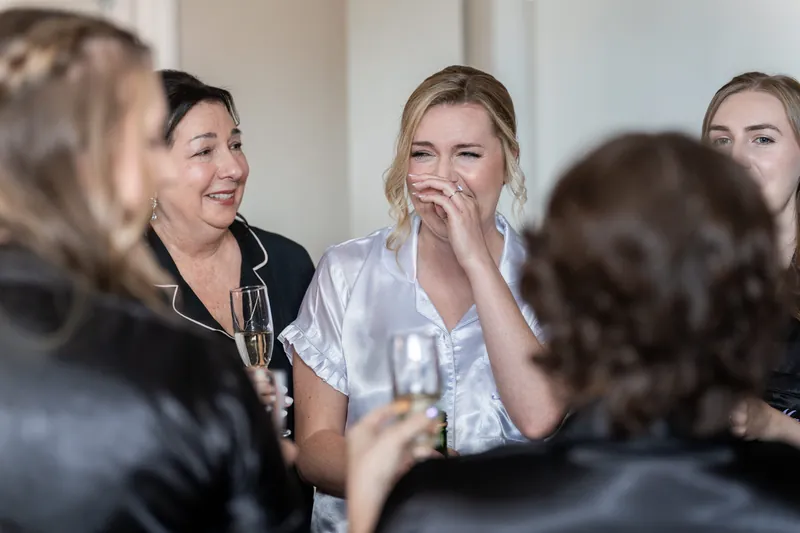Sarah beams while surrounded by friends in a tight circle, all sharing laughter and conversation before the ceremony.