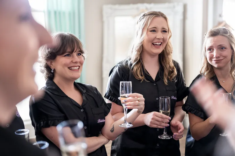 Three women in black shirts hold champagne glasses and smile at The White Room during the reception.