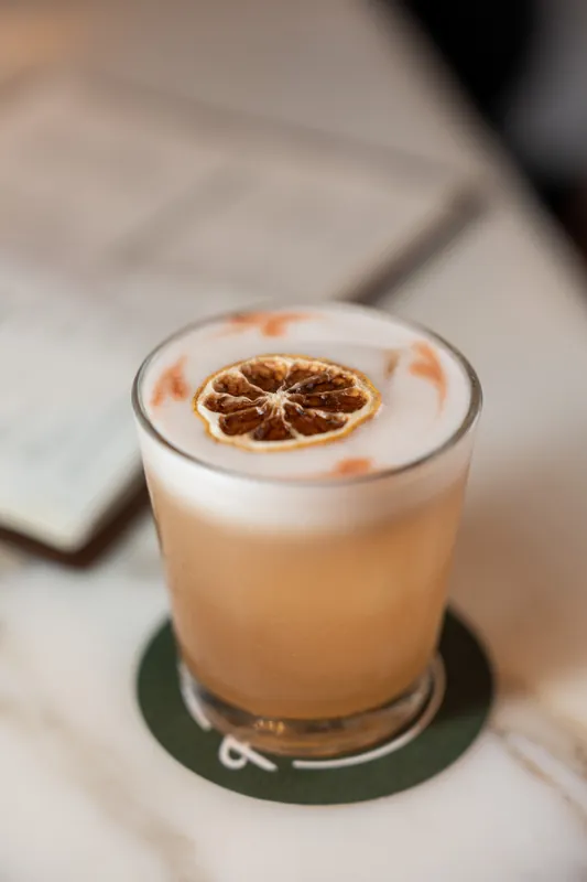 A cocktail with a dried citrus slice garnish sits on a green coaster at the reception.