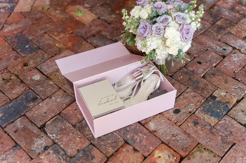 A pink box holding a menu card rests beside a small bouquet on a brick pathway.