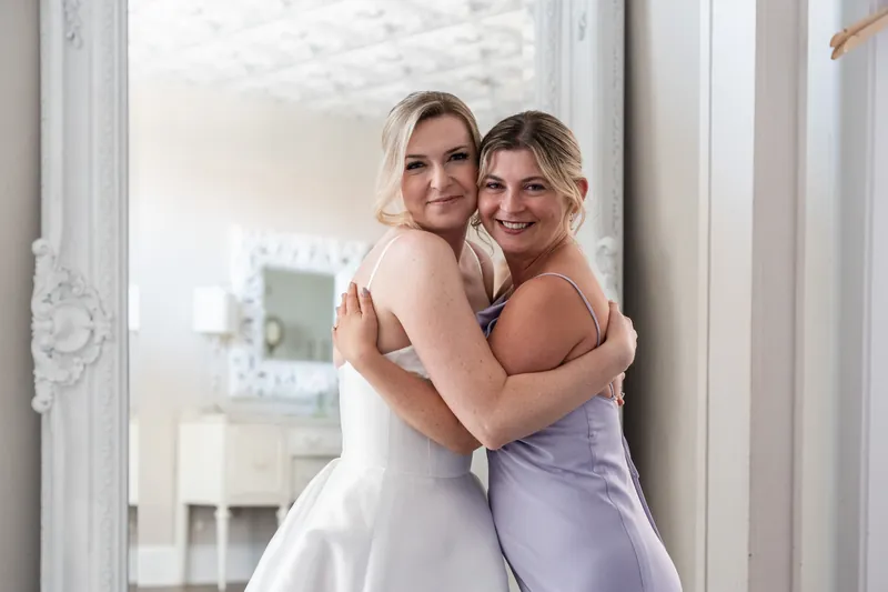 Sarah and a companion in lavender embrace and smile while standing in an ornate doorway.