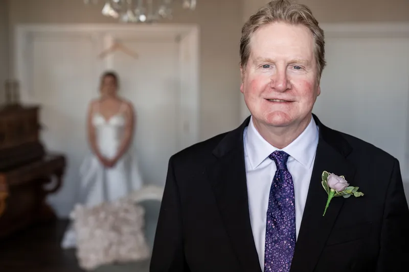 Tim wears a dark suit with a purple tie and white boutonniere, smiling toward the camera.