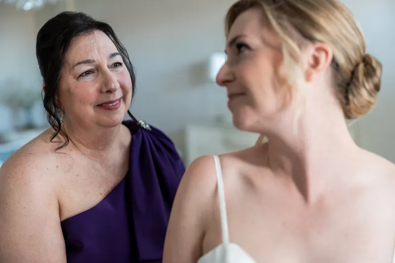 Two women in formal attire chat warmly at The White Room, one in purple and the other in a white slip dress.