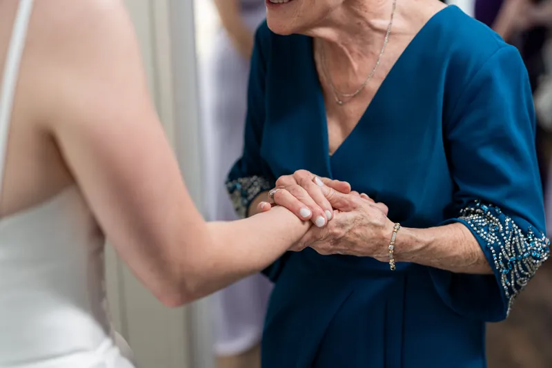 A woman in a navy cardigan carefully fastens a bracelet around Sarah's wrist.