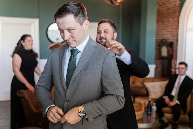 Tim adjusts his suit jacket cuffs as groomsmen assist with his wedding attire.