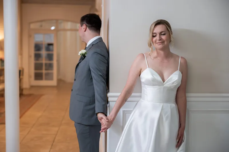 Sarah and Tim hold hands in a hallway at The White Room, she in a white dress and he in a gray suit.