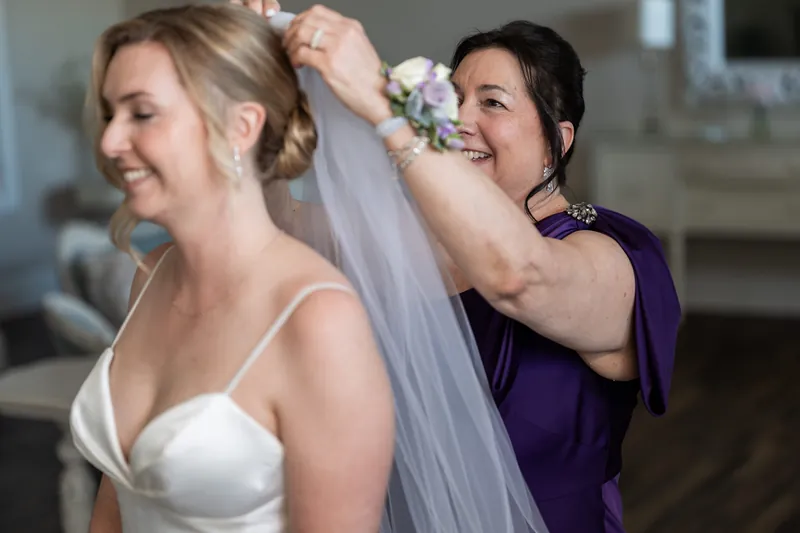 A woman in purple adjusts Sarah's veil as she stands in her wedding dress at The White Room.