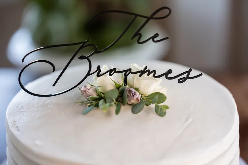 A scripted "The Grooms" cake topper adorns the top tier of the white wedding cake with small floral accents.