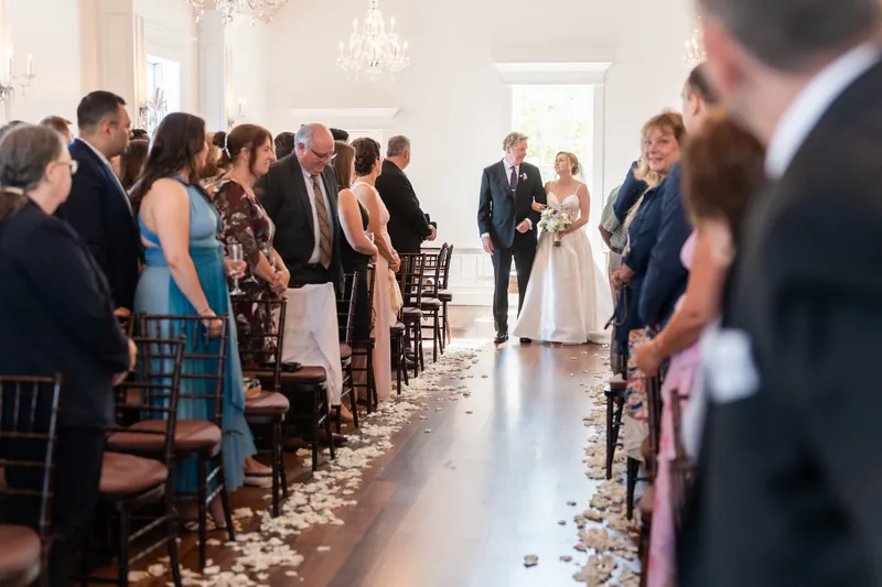 Sarah and Tim stand at the altar beneath a crystal chandelier as wedding guests watch from wooden chairs lining the aisle