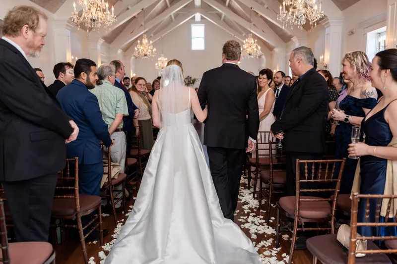 Tim and Sarah face each other at the altar, surrounded by guests in formal attire inside the elegant white chapel.