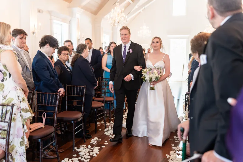 Tim walks down the aisle with Sarah's parent as guests rise to their feet in the chapel.