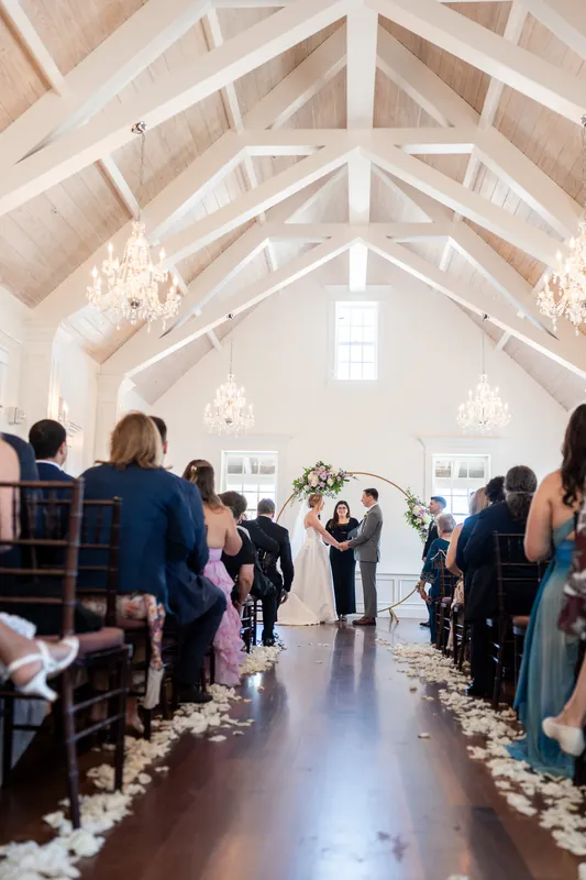 The couple stands at the altar under vaulted ceilings and chandeliers as guests fill both sides of the aisle during