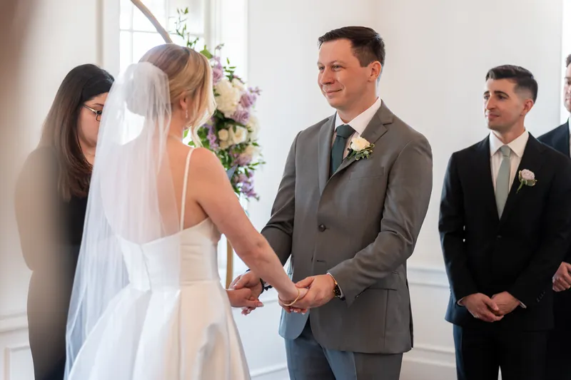 Sarah and Tim hold hands at the altar as guests and attendants look on during their ceremony at Villa Blanca.