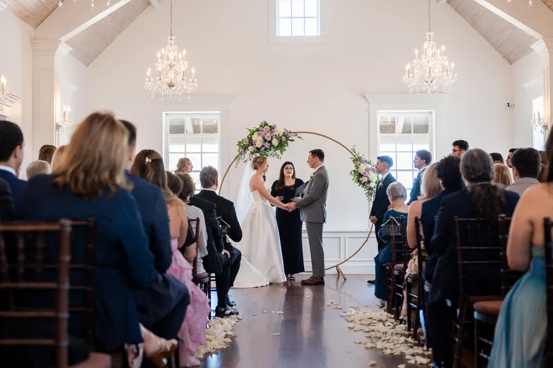 Sarah and Tim exchange vows beneath a floral arch in the bright, chandelier-lit ceremony space at Villa Blanca.