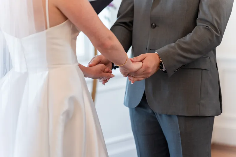 Tim slides a wedding band onto Sarah's finger as she holds his hand during their ceremony.