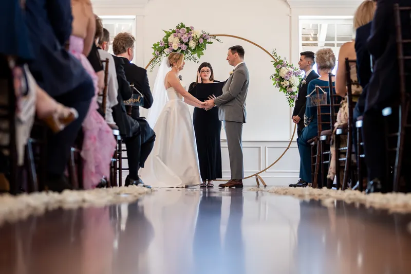 Sarah and Tim stand together at the altar while an officiant conducts their ceremony, framed by guests on both sides.