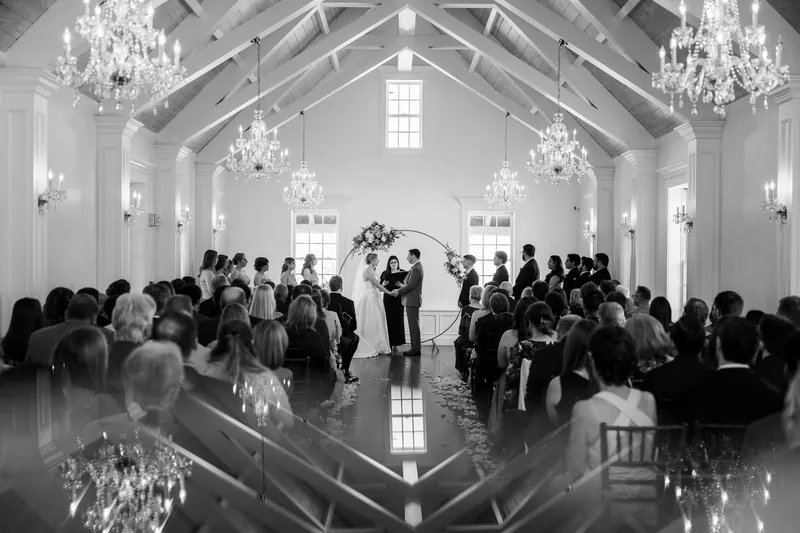 Guests fill a bright white chapel with soaring ceilings and chandeliers, watching the ceremony unfold.
