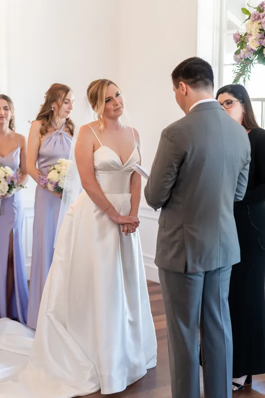 Tim holds Sarah's hands during their ceremony while attendants and guests look on.